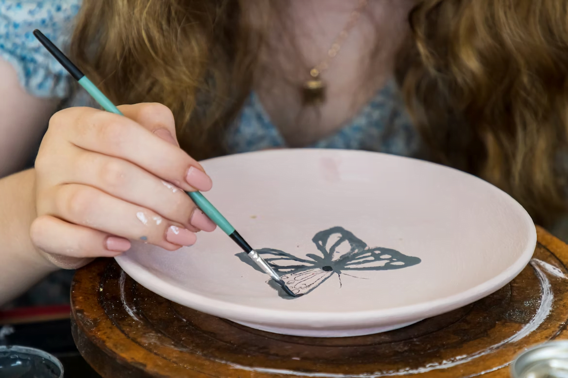 a woman painting a butterfly on a ceramic plate
