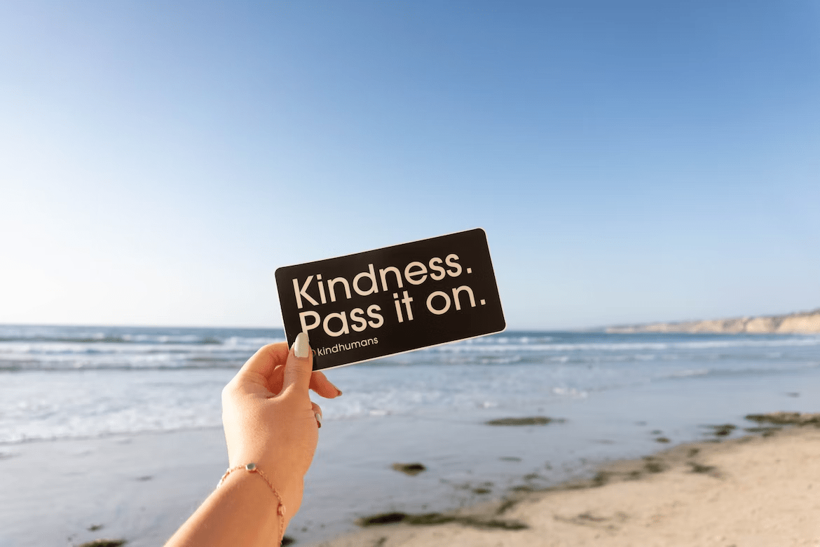 a person holding up a card that says "kindness pass it on."