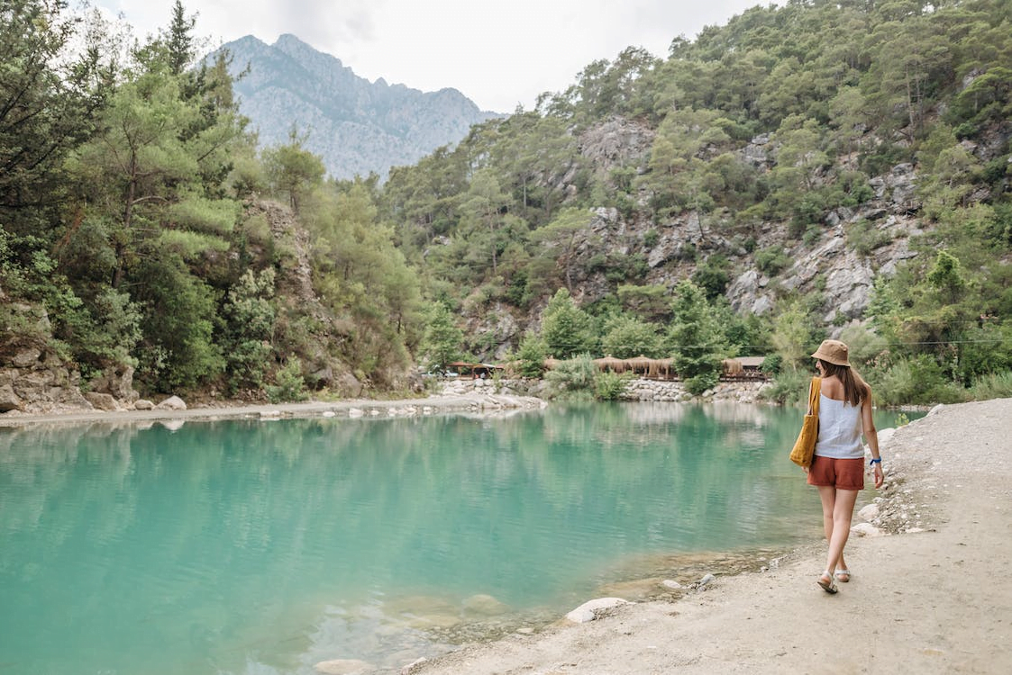 a woman walking on riverbank beside a mountain