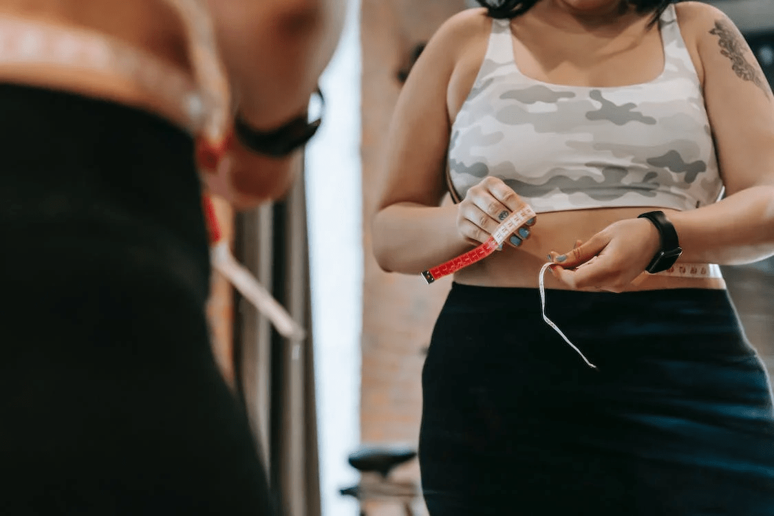 a woman measuring waist with tape in gym
