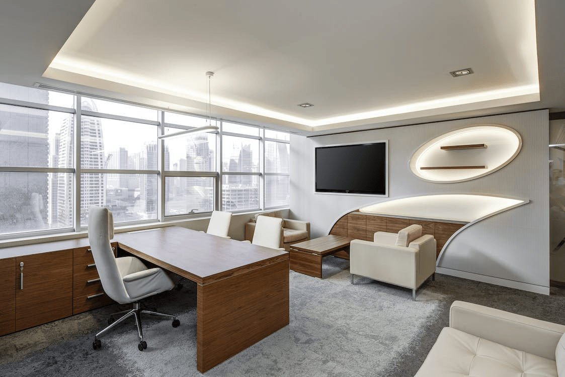 gray office rolling chair near brown wooden desk in front of flat screen TV on white painted wall