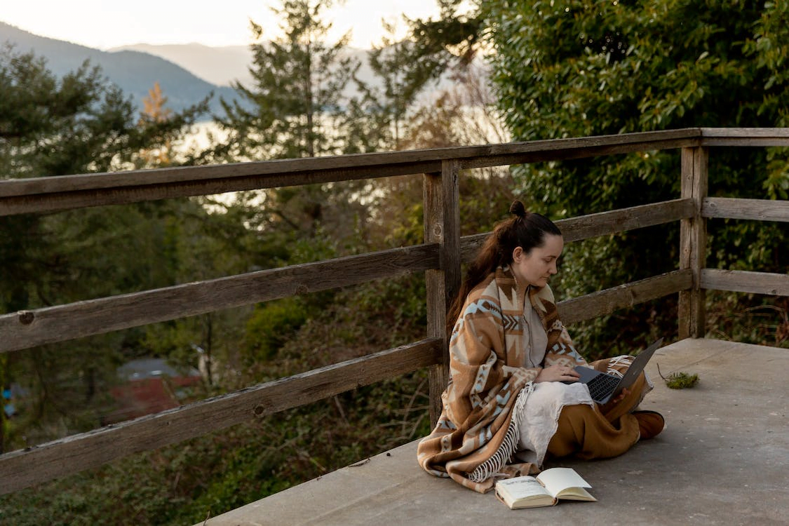 a woman typing on laptop while sitting on veranda near mountains
