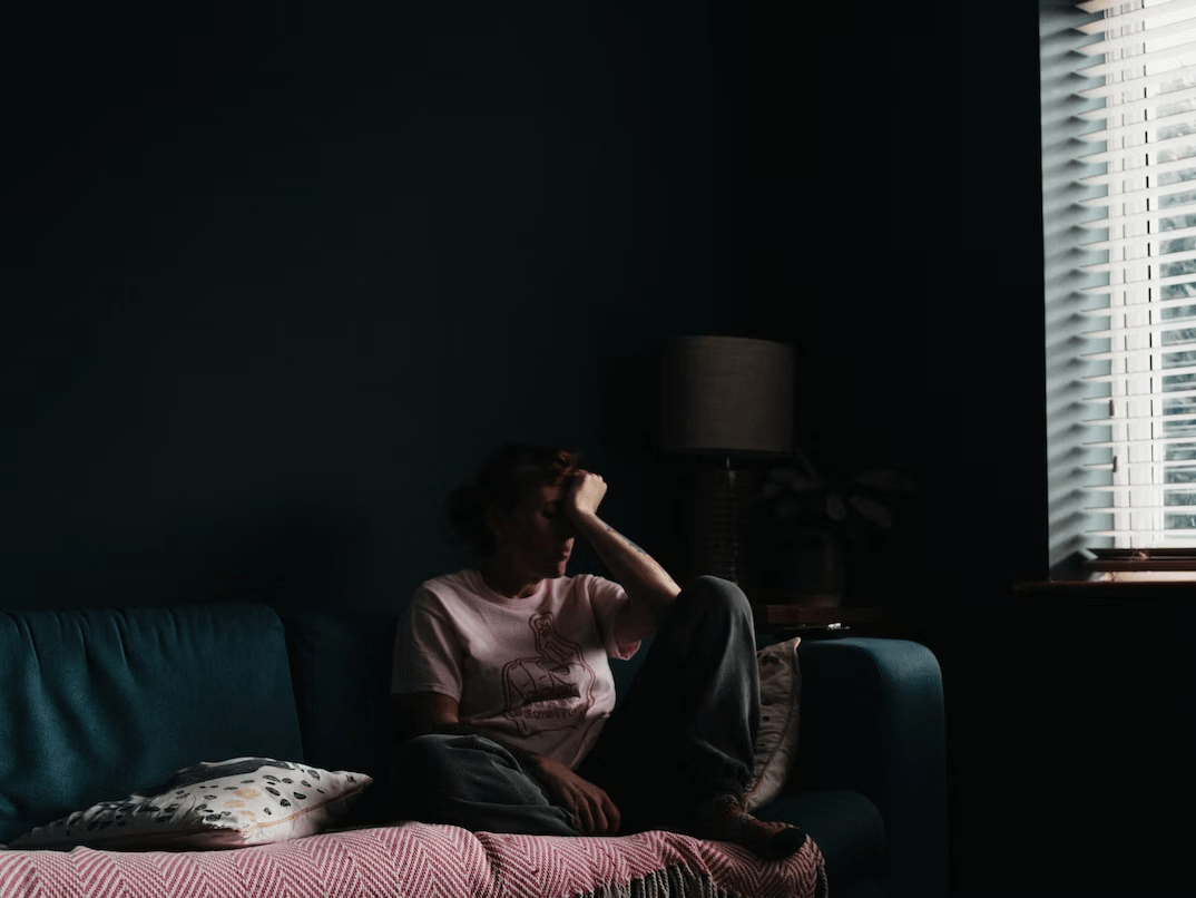 a man sitting on a couch in a dark room with his hand on his face