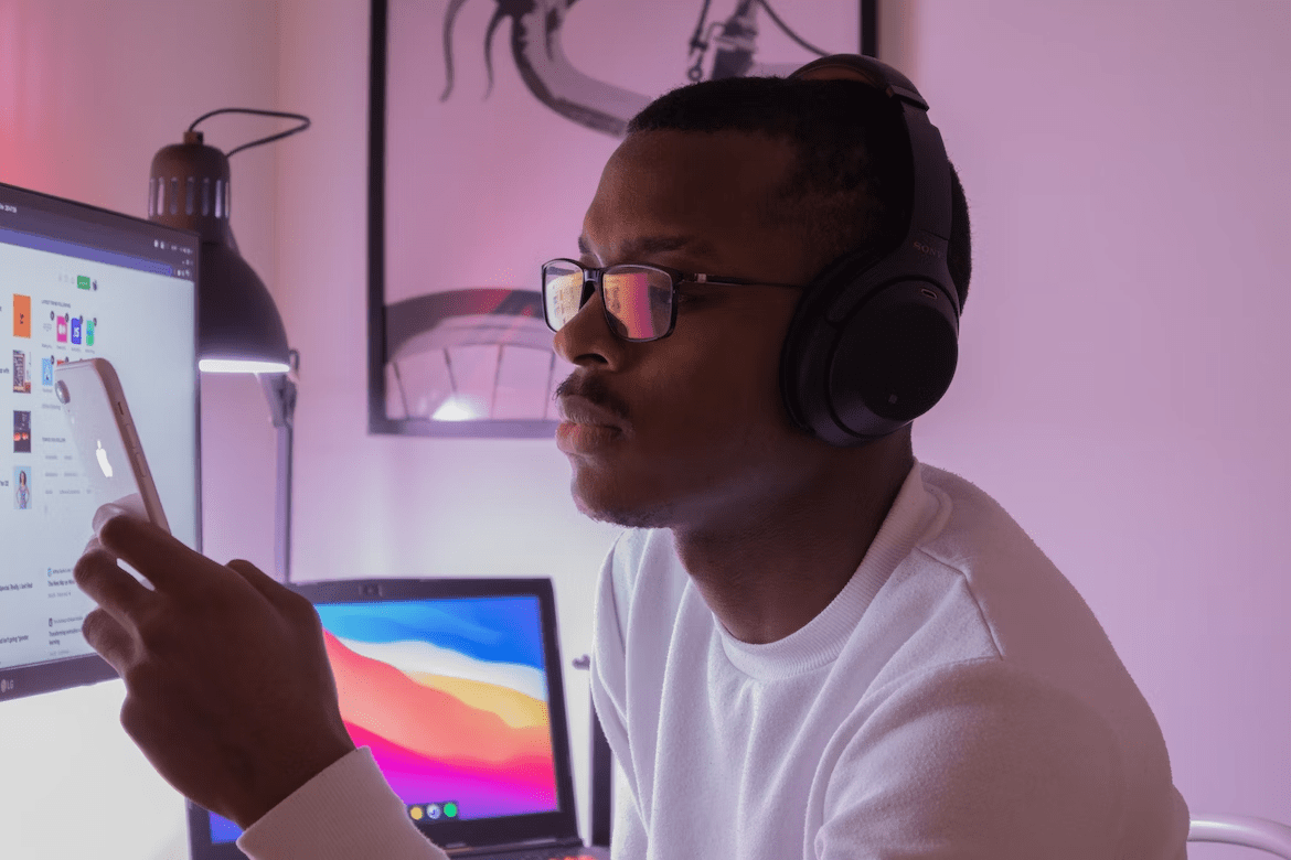 a man wearing headphones in front of a computer screen, using his phone