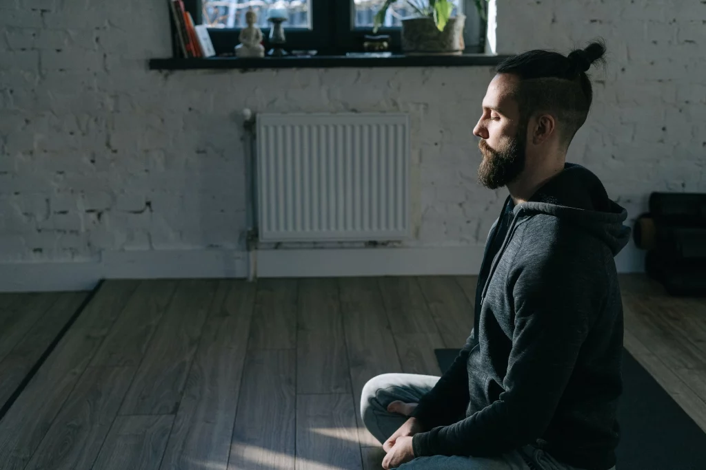 a man in hoodie sweater meditating over a yoga mat