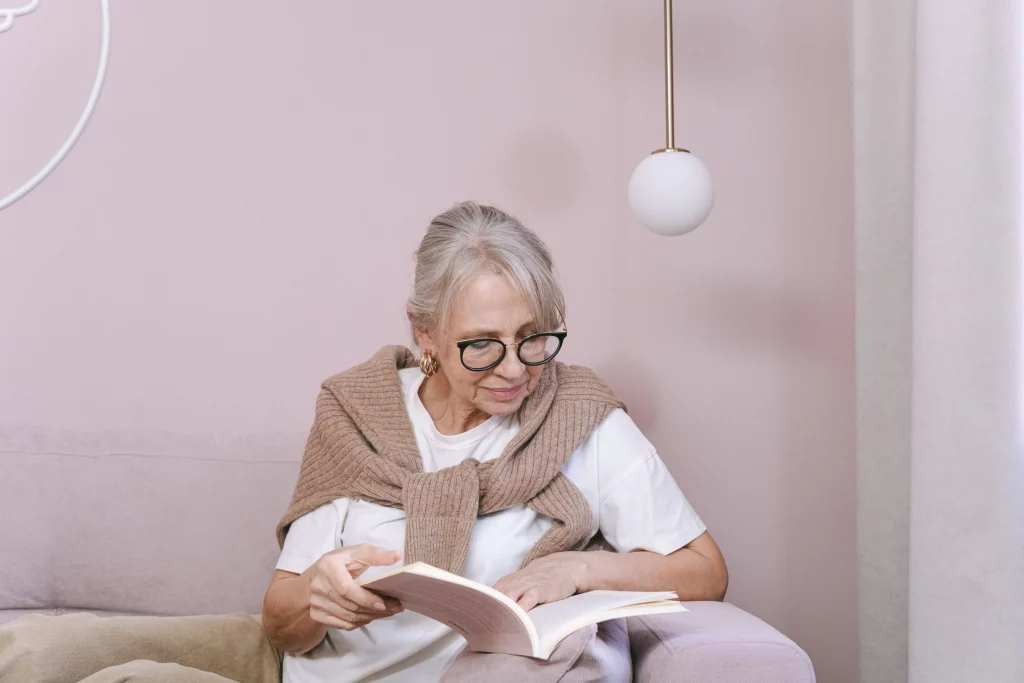 a woman in eyeglasses reading a book on pink sofa