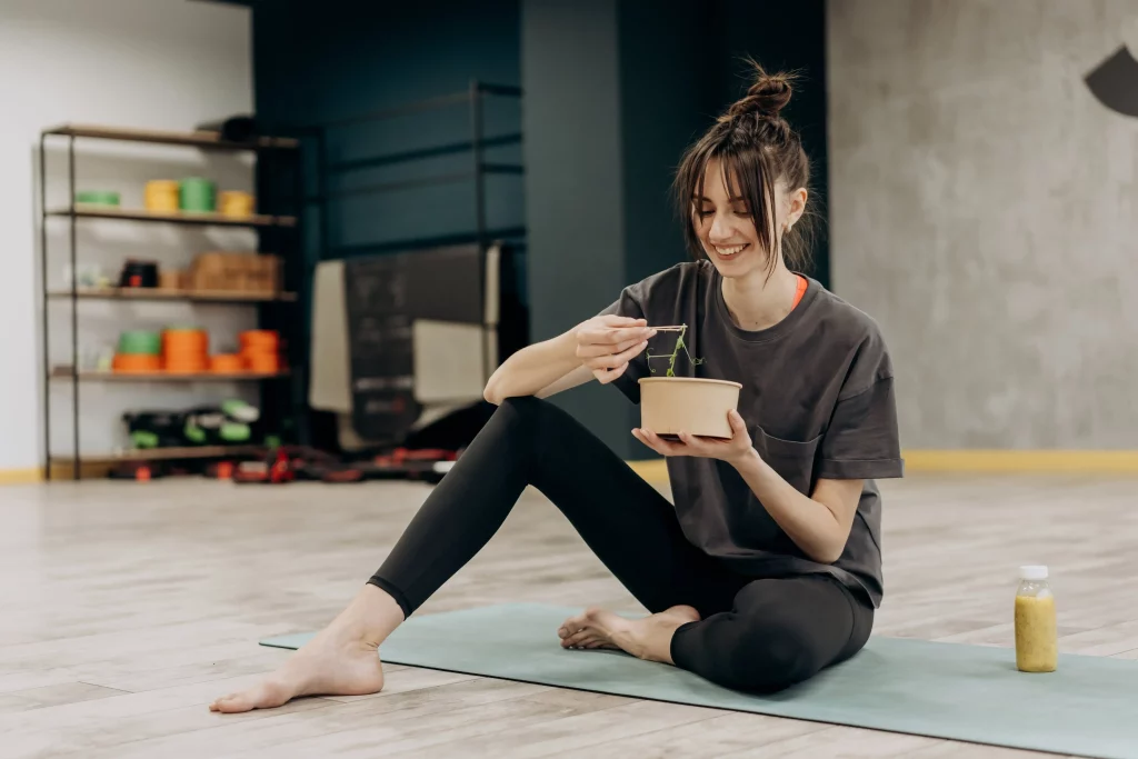 a woman sitting on a yoga mat, eating healthy food