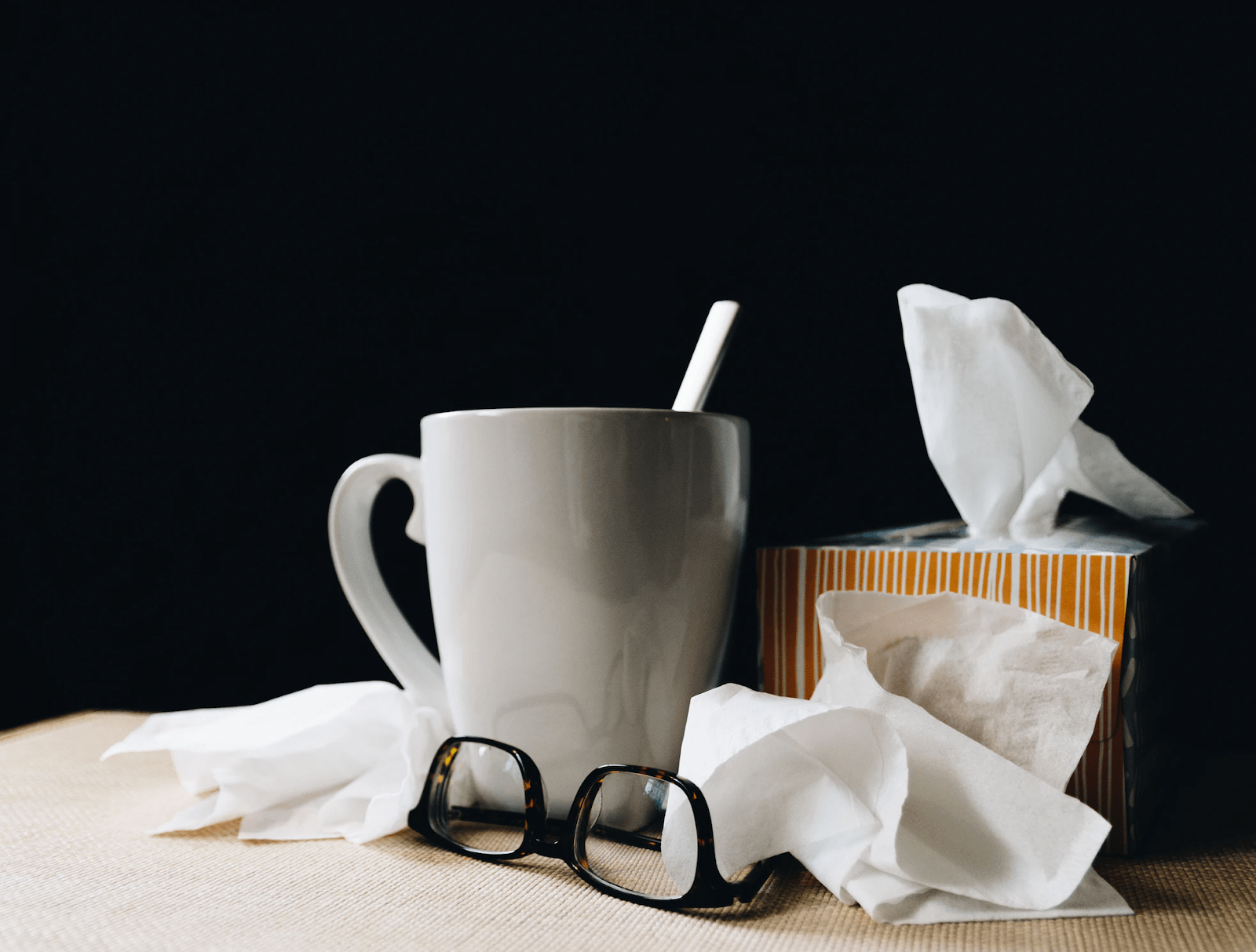 a mug, eyeglasses, tissues, and used tissues on a table
