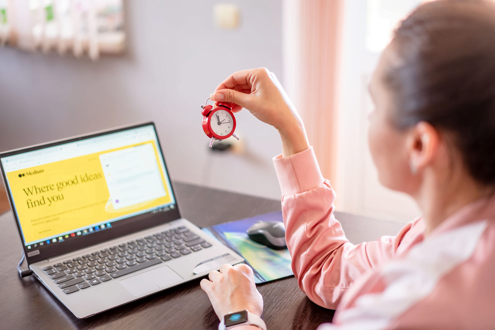 a woman holding a red mini clock in front of the desk with a laptop