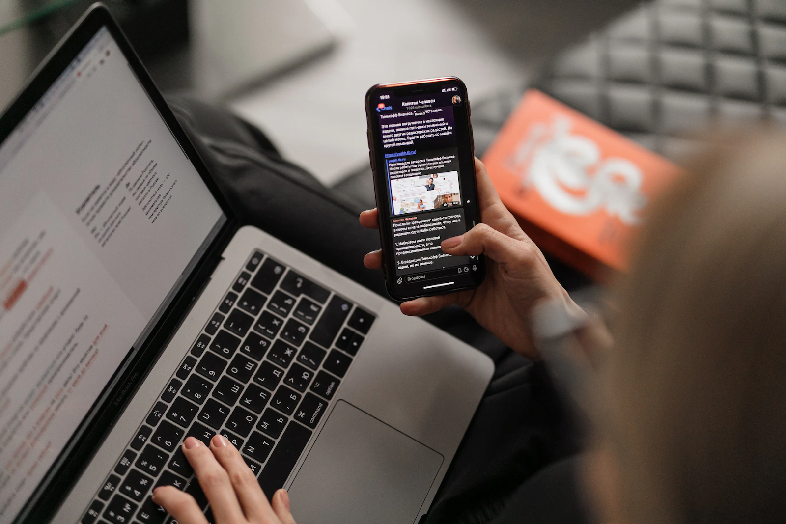 woman on leather couch working at a laptop while browsing her phone