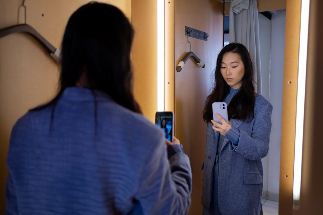 woman wearing coat taking picture in a mirror