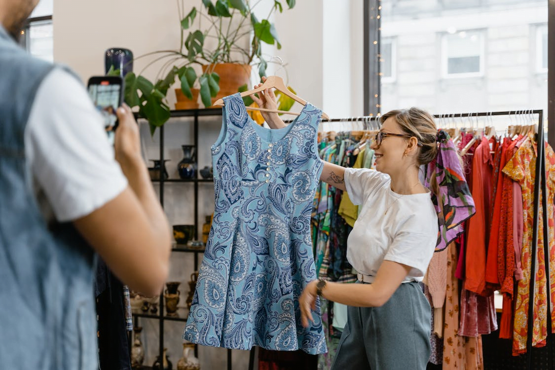 a woman holding a blue dress and a man taking a photo of it