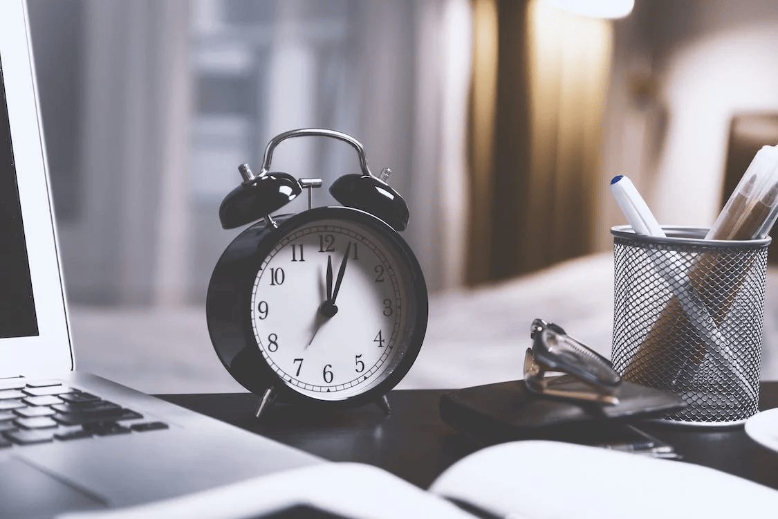 a black twin bell alarm desk clock on table beside a laptop