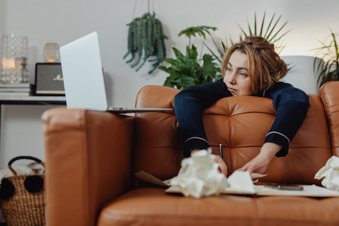 a woman in pajamas looking at her laptop with her arms resting on the cushions