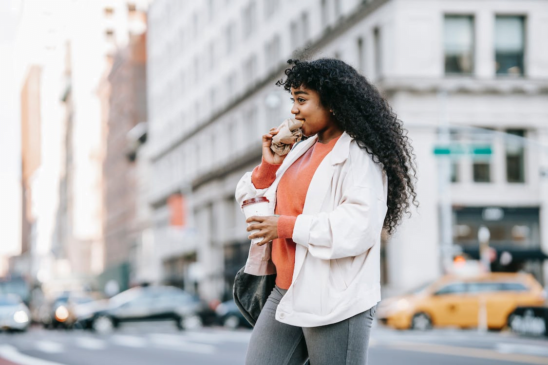 a woman crossing the road while biting a sandwich