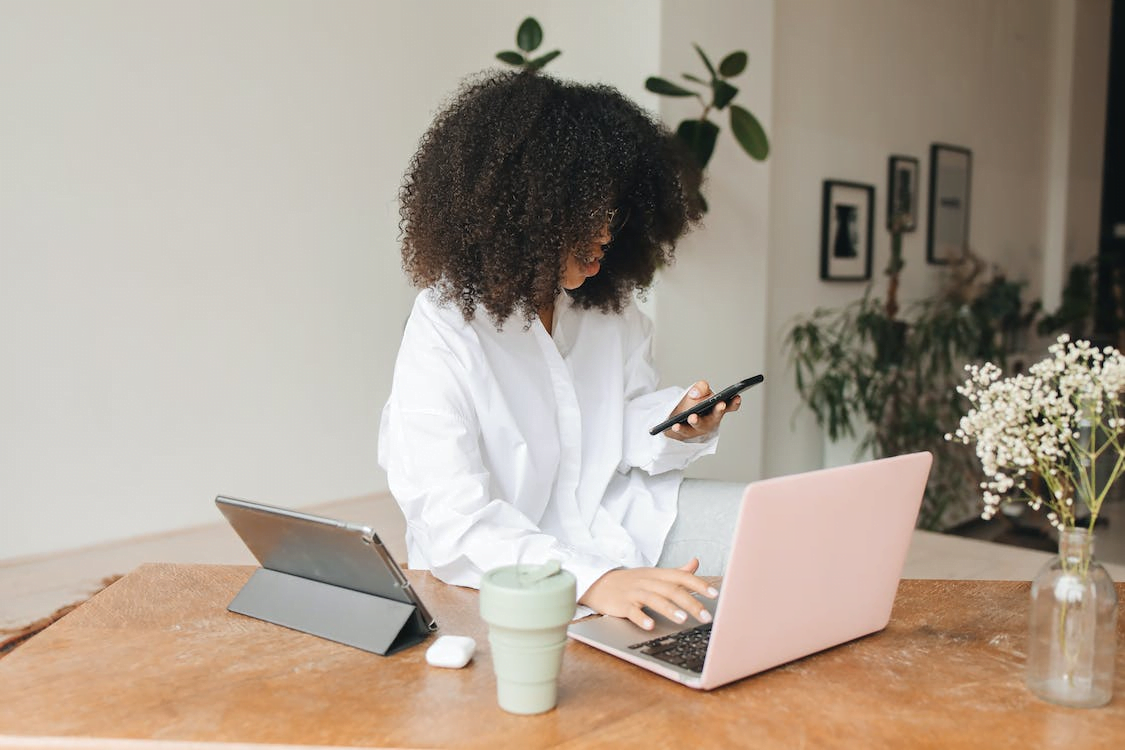 a woman holding a cellphone and typing on a laptop