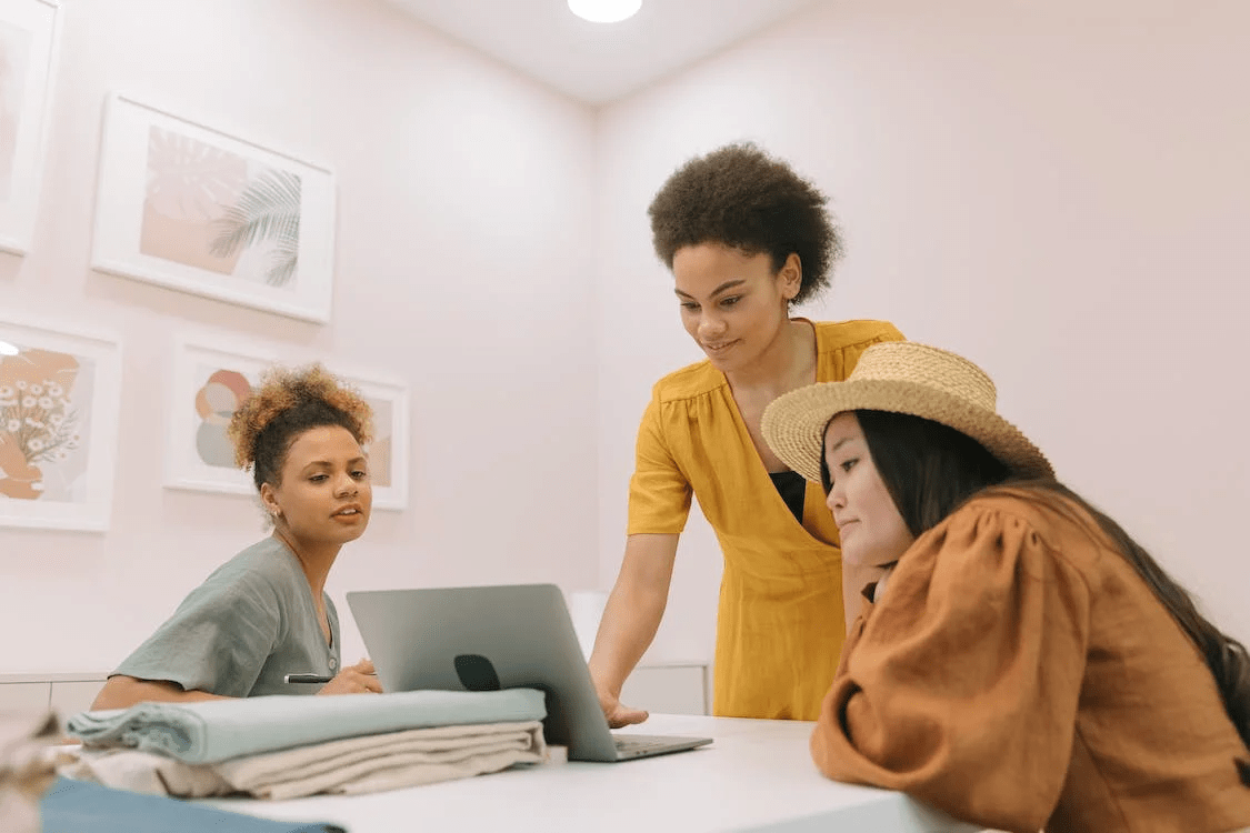 three women work together on a laptop in a shared space