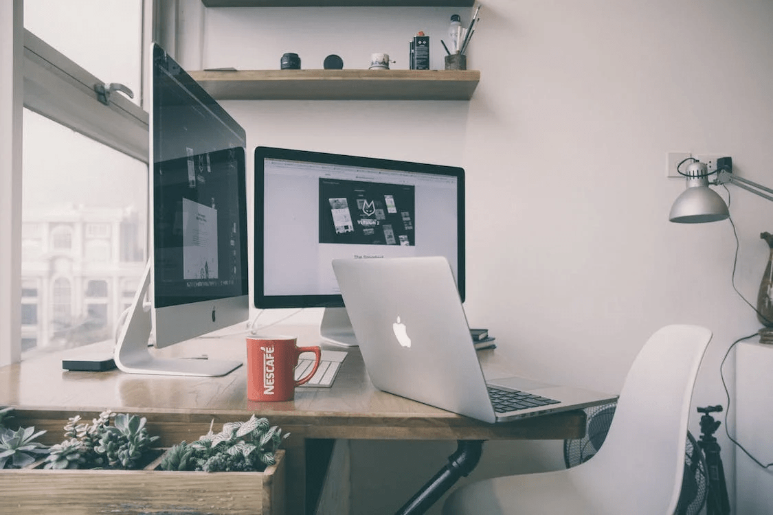 a well-lit workspace with dual monitors, laptop, and a coffee cup on the desk.