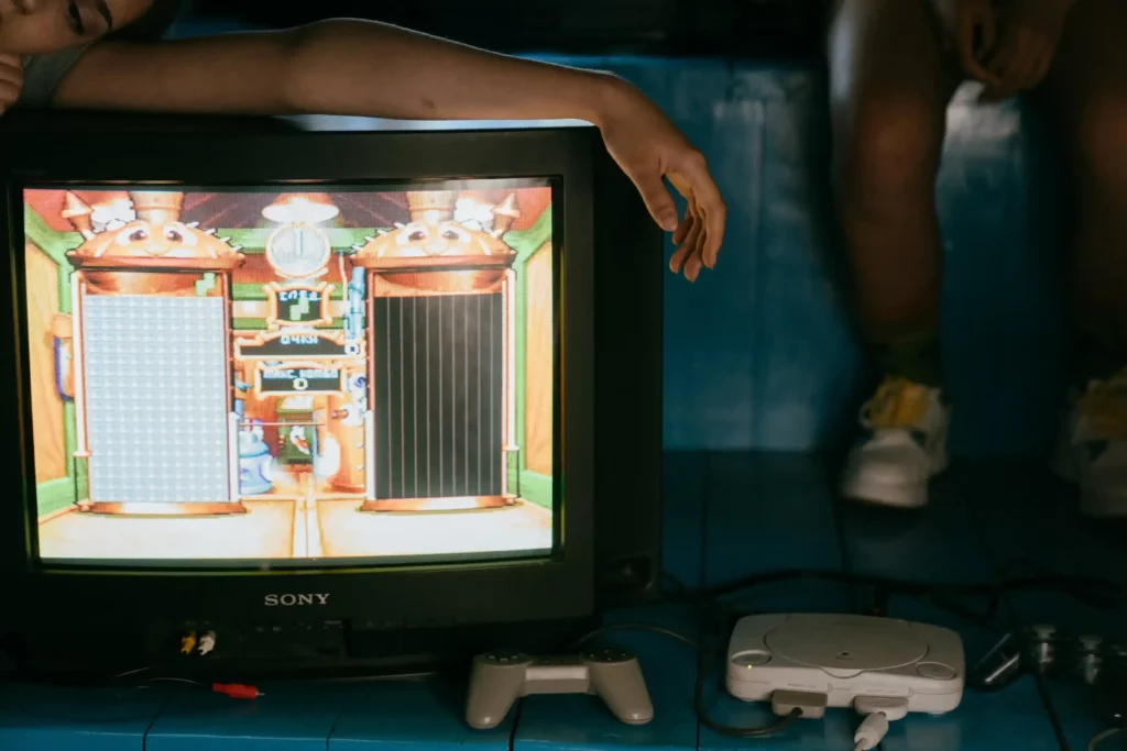 image of video game on TV screen, with a person's arm laying on topic and a gaming console towards the bottom of the image 